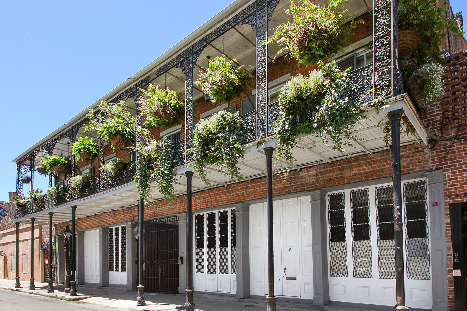 French Quarter three-story brick building with fern-draped ornate iron balconies — sold by Patrick Knudsen New Orleans